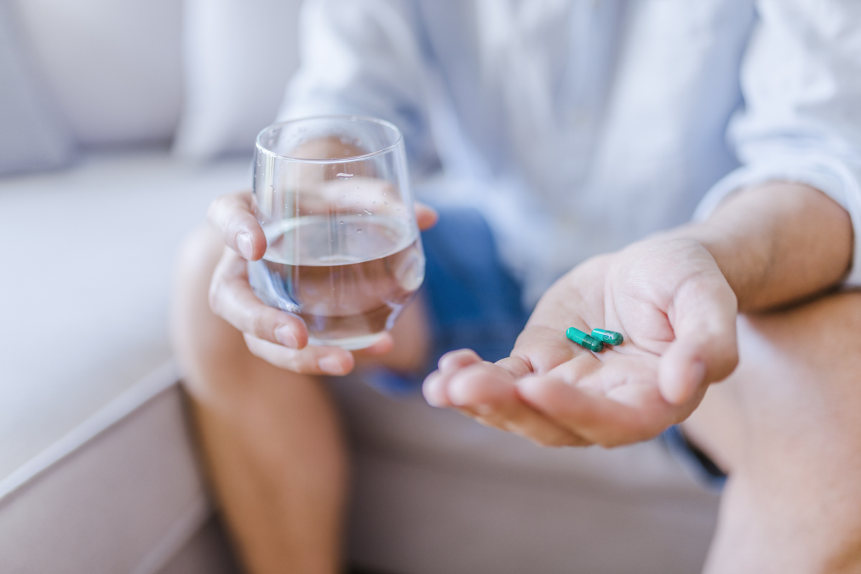 Person holding glass of water and green capsules for medication assisted treatment in Spokane Valley, WA