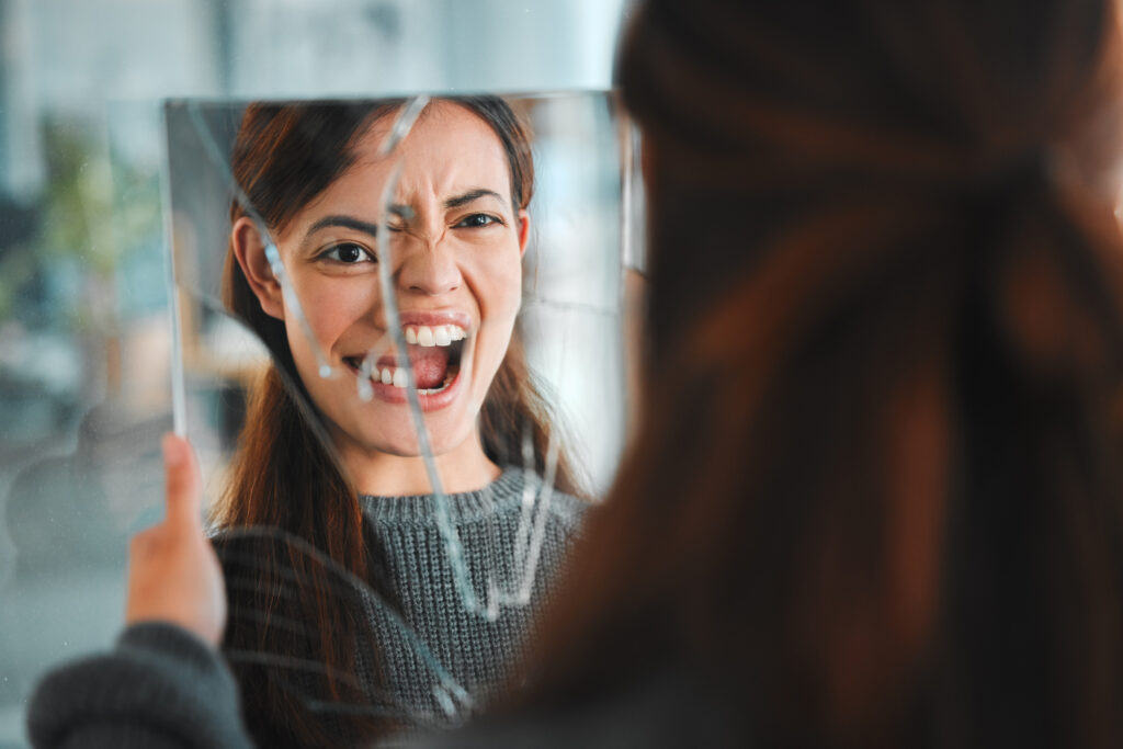Woman holding a broken mirror with distressed reflection, symbolizing bipolar and addiction treatment support in Spokane, WA