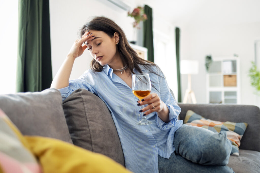 Woman sitting on a couch holding a glass of wine, experiencing stress and fatigue, effects of alcohol withdrawal in Spokane Valley, WA