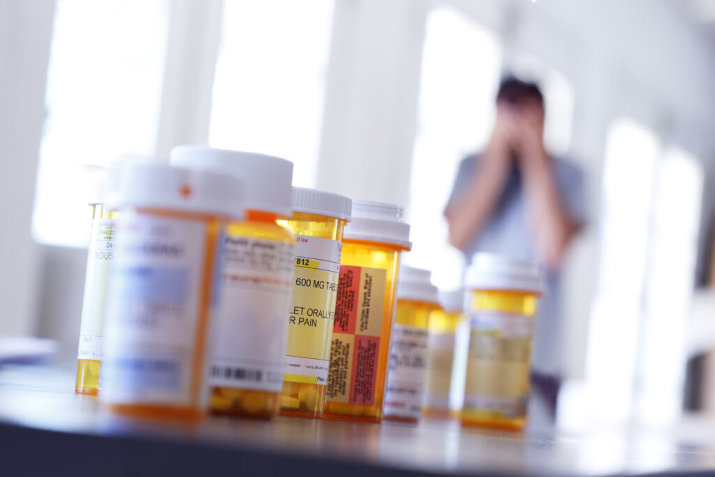 row of prescription pill bottles with a distressed person in background, highlighting prescription drug addiction resources in Spokane Valley, WA and greater Washington State