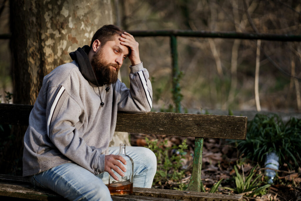 Man sitting on a park bench with alcohol bottle, showing signs of stress and addiction Spokane, WA