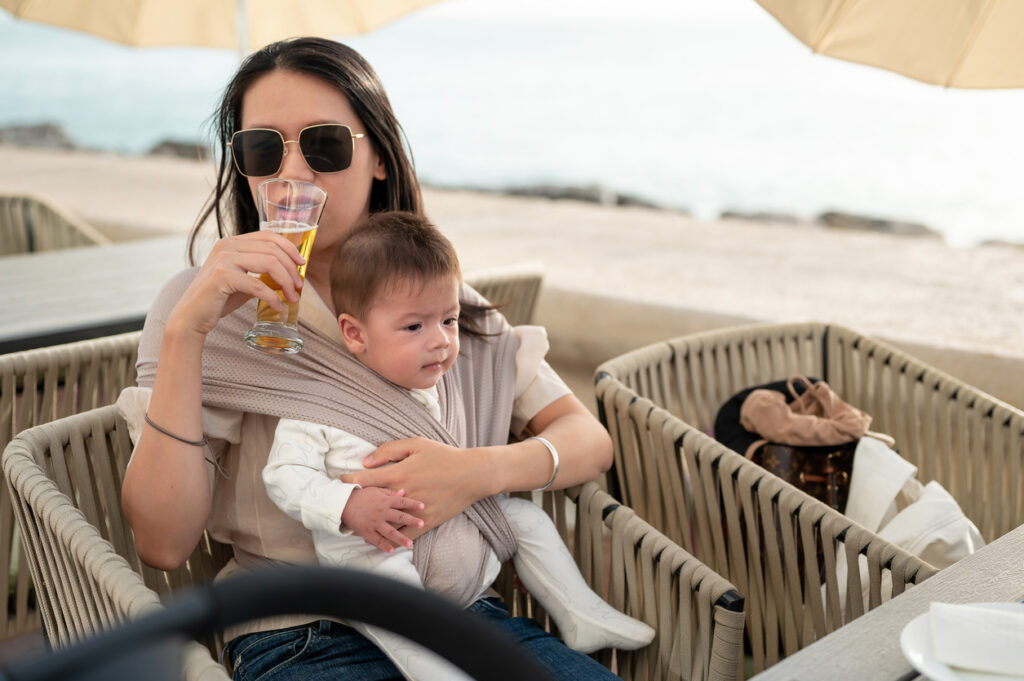 young mother drinking beer while holding baby at an outdoor café, raising alcohol and breastfeeding safety questions in Spokane and Spokane Valley, Washington State