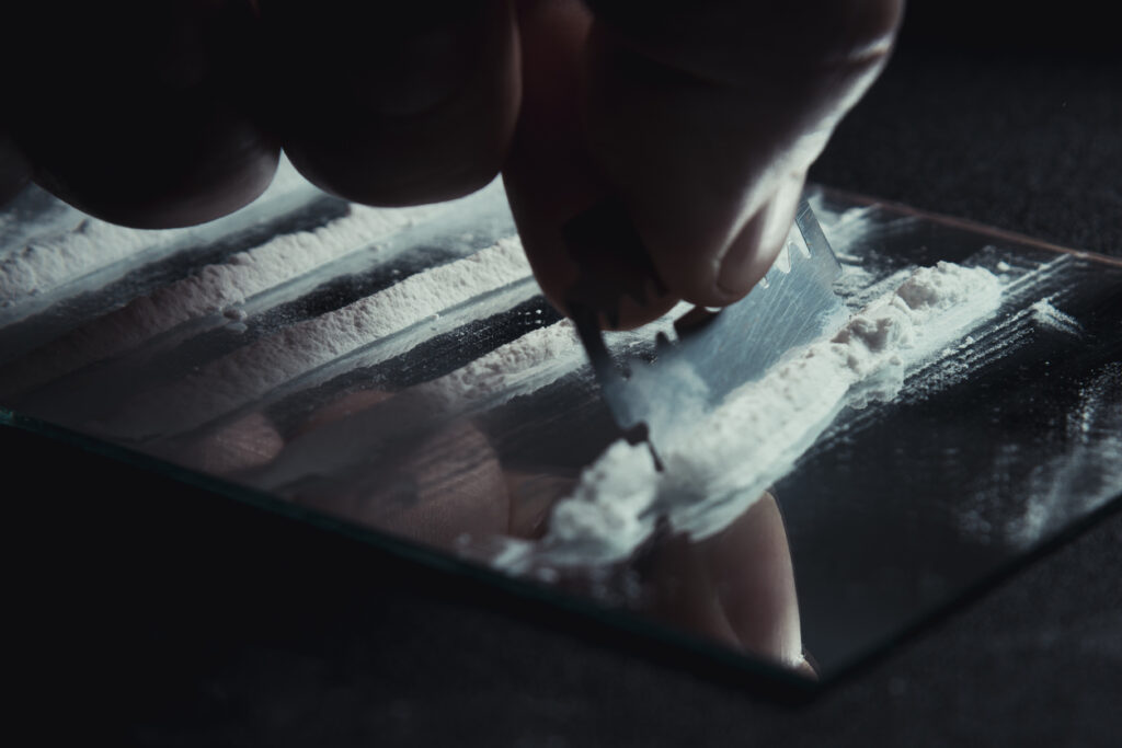 close-up razor cutting lines of white powder on glass, depicting cocaine side effects like elevated heart rate, nasal damage, and anxiety in Washington State, Spokane, and Spokane Valley