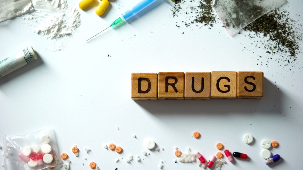 flat lay of pills, powder, syringe, and the word “DRUGS” spelled with wooden blocks, representing common drug slang terms across Washington State, including Spokane and Spokane Valley