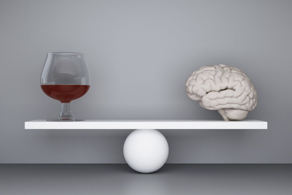 A glass of alcohol and a human brain model balanced on a scale, symbolizing how alcohol affects brain health in Spokane WA