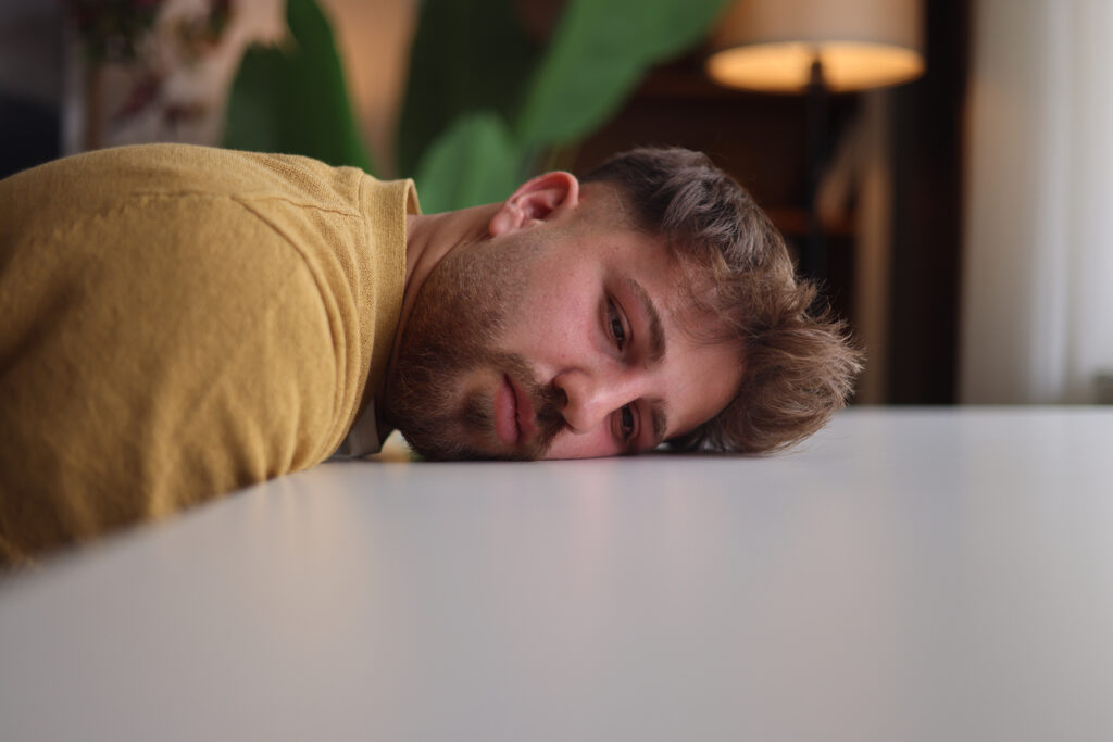 young man lying exhausted on table after drinking, visualizing the depressant effects of alcohol on energy and motivation in Washington State (WA), including Spokane and Spokane Valley