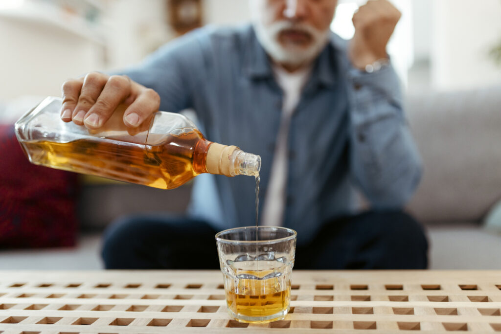 Older man pouring whiskey into a glass symbolizing alcoholism as a mental health disorder in Spokane WA