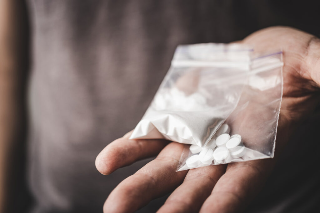 Hand holding zip bag with white powder and pills illustrating snorting adderall misuse and overdose concerns; resources highlighted for Spokane Valley, Washington State (WA)