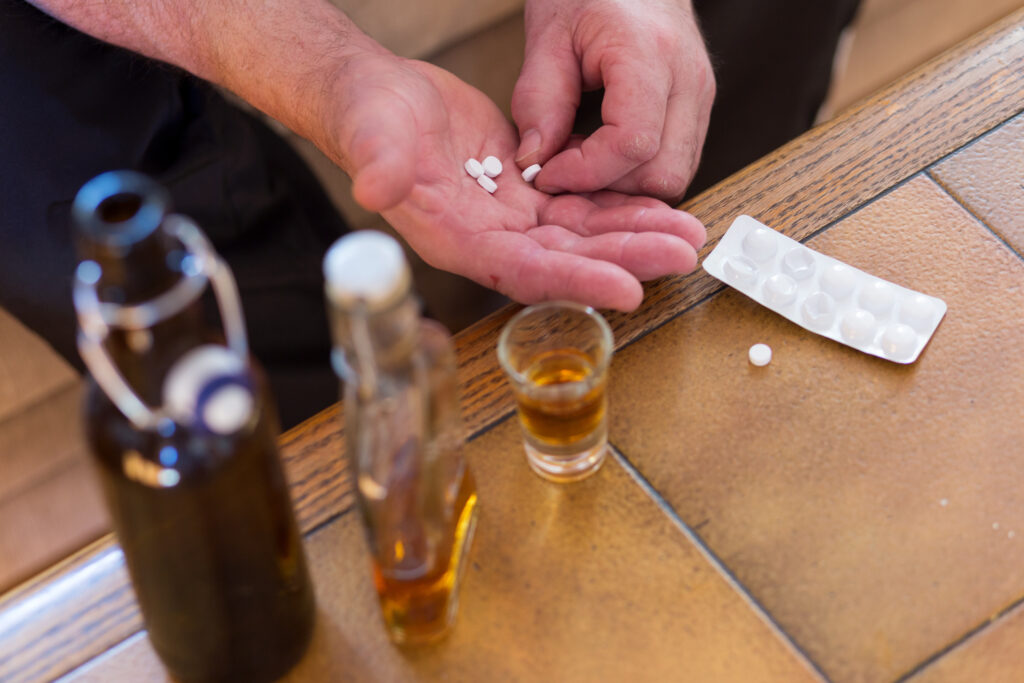 Person holding white pills with bottles of alcohol on a table showing the dangers of mixing Zoloft and alcohol in Spokane WA