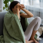 A woman sitting on a sofa covering her eyes representing stages of depression