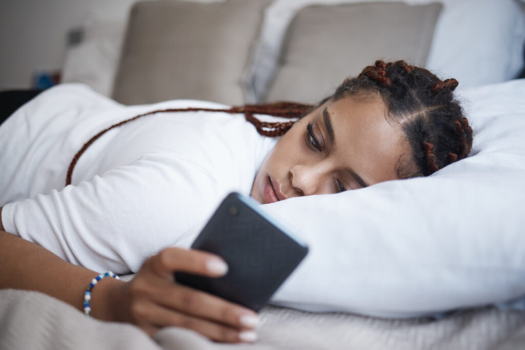 Young woman lying in bed scrolling on phone, signs of mild depression in Spokane, Washington State (WA)