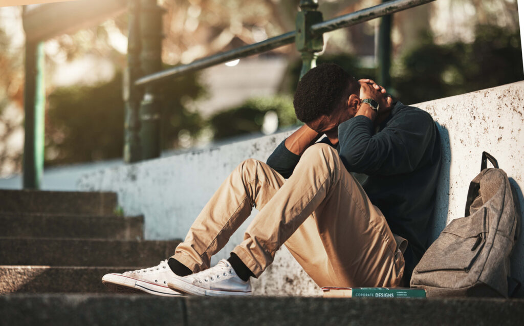 Student sitting on outdoor steps with head in hands, signs of mild depression in Spokane, Washington State (WA)