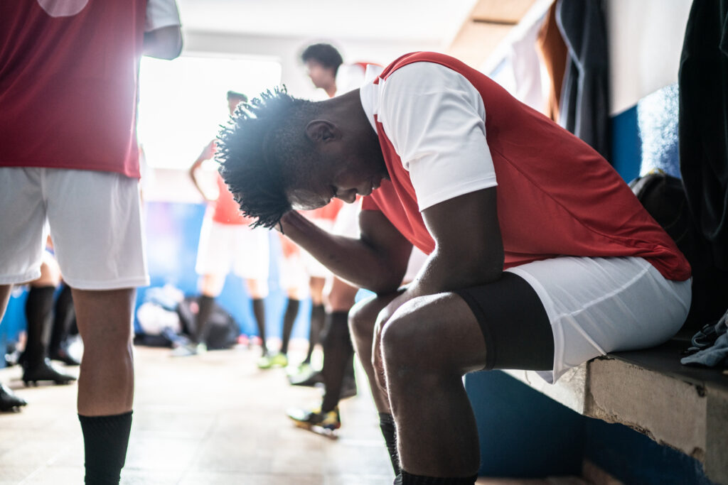 Athlete in locker room with head down, experiencing performance anxiety before game in Spokane, WA