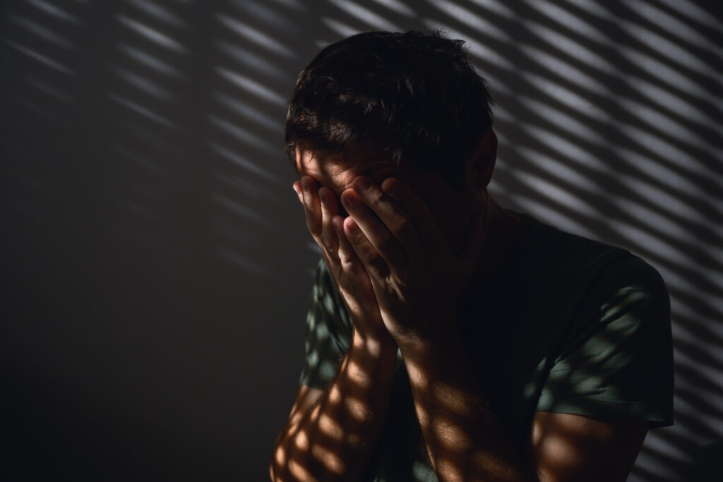 Man sitting in shadow with hands on face representing emotional struggle during Men’s Mental Health Month in Spokane WA