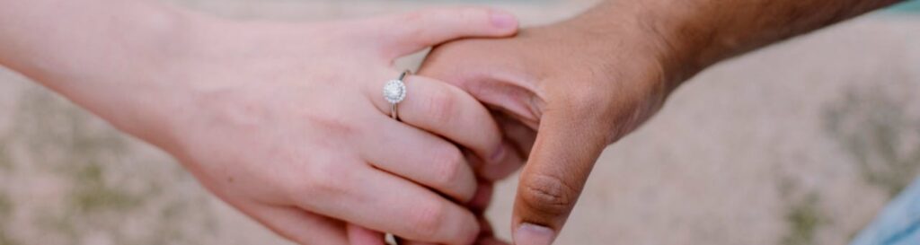 A close up photo of hands of a man and woman holding each other with a wedding ring on the woman's hand representing divorce and mental health