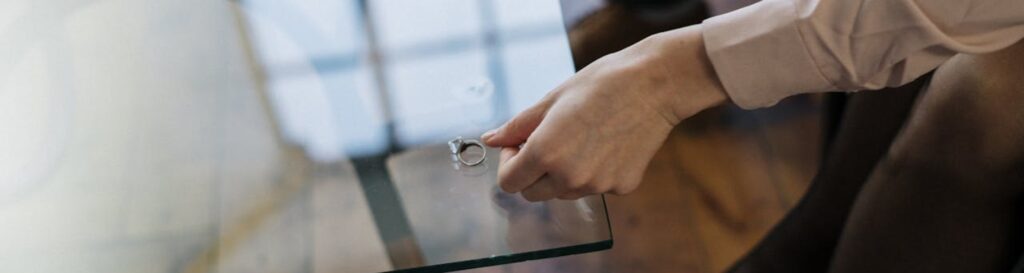 A hand placing a wedding ring on a glass table