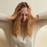 A woman experiencing panic attack screaming and holding her head