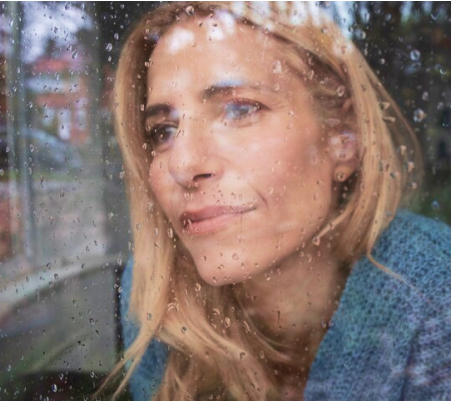 A sad woman looking outside a window covered in raindrops