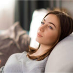 A woman sitting on a sofa looking at a distance needing CBT for anxiety disorders