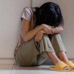 A depressed woman sitting on the floor leaning her head on her knees