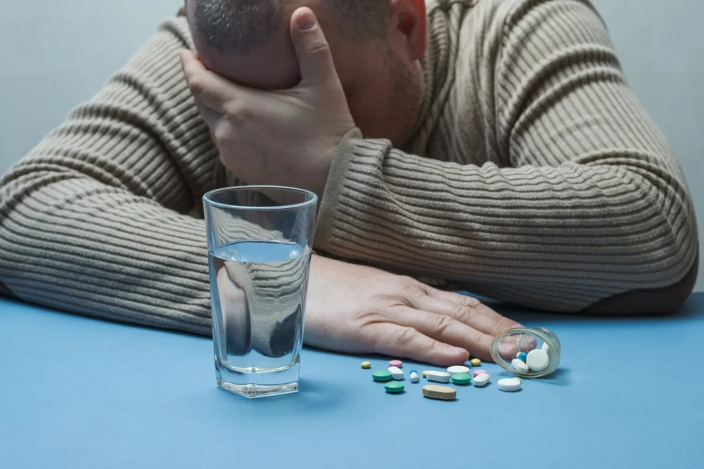Man holding his head in distress beside a glass of water and spilled pills, representing propranolol for anxiety treatment in Spokane WA