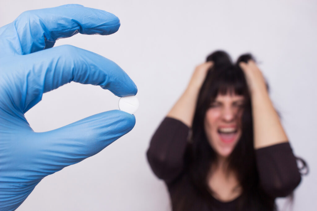 Gloved hand holding a white pill with a distressed woman in the background, symbolizing propranolol for anxiety treatment in Spokane WA