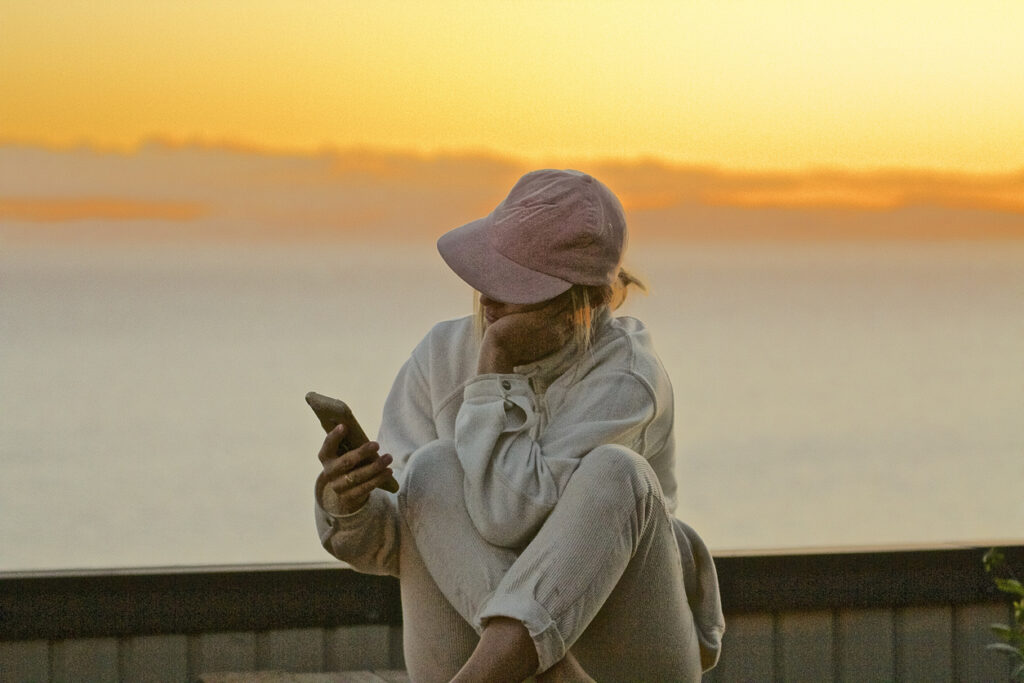 Person sitting outdoors at sunset looking at a phone with a thoughtful expression, symbolizing reflection on adhd vs autism awareness in Spokane Valley Washington