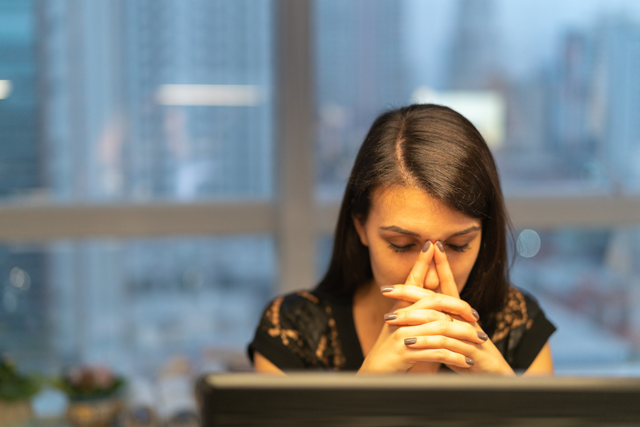 Woman sitting at a desk with her head in her hands looking stressed or overwhelmed, representing focus and emotional differences in adhd vs autism in Spokane Valley Washington